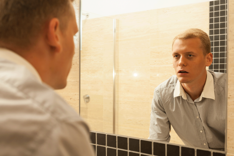 an adult man is in a public restroom looking at his reflection in a mirror wondering if he is showing signs of a relapse