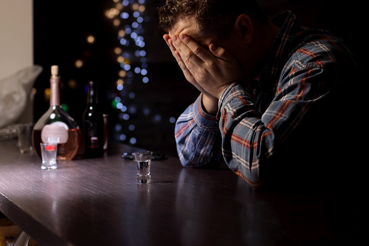 a person holds their hands to their face appearing to be distraught and possibly dealing with depression and alcohol abuse